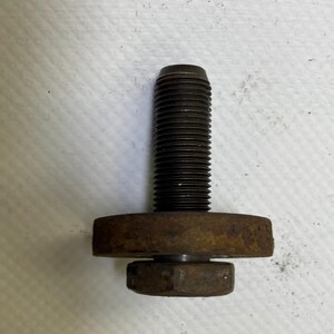以下が含まれることがあります： ねじ山のあるシャフト、円形のワッシャー、六角ナットが付いた、錆びた濃い色の金属ボルト。ボルトの頭は円筒形で、部品は経年劣化の兆候を示しています。