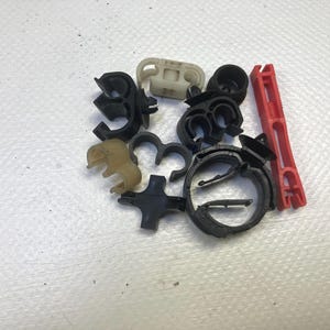 May include: A collection of various automotive plastic clips and fasteners in black, tan, and red. The assortment includes hose clamps, wire retainers, and other small parts, likely for vehicle repair or maintenance.