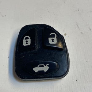 May include: Black car key fob with three buttons. The buttons have symbols for lock, unlock, and a car with a trunk open.