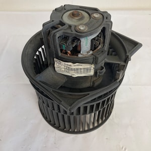 Puede incluir: Motor de soplador de calefacción de coche negro con una jaula de ventilador de plástico negro y una etiqueta que dice "Sah. GMV".