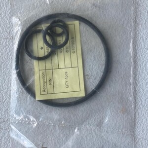 May include: A set of four black rubber O-rings of varying sizes enclosed in a clear plastic bag. A yellow paper label inside the bag displays the text Recognition, P/N, QTY: 4pcs, and various technical specifications including Φ2*Φ3, Φ16, and Φ10*Φ2.5.