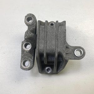 May include: Two gray metal automotive parts. One part is a bracket with three circular holes. The other part is a rectangular housing with a circular hole and vertical ridges. Both parts have a worn, used appearance.