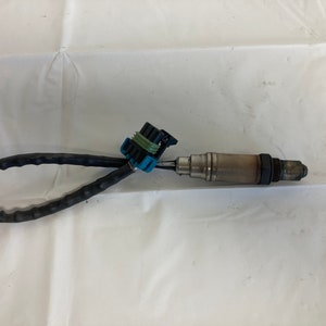 Może przedstawiać: Czujnik tlenu z czarnym kablem i niebiesko-zielonym złączem. Czujnik służy do pomiaru ilości tlenu w spalinach pojazdu.