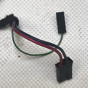 Könnte beinhalten: Nahaufnahme eines schwarzen elektrischen Steckers mit drei Drähten: rot, schwarz und grün. Die Drähte sind mit einem schwarzen Stecker mit einer kleinen schwarzen Abdeckung verbunden.