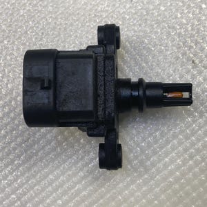 May include: A black automotive sensor with a rectangular body and multiple protruding elements. The sensor has a cylindrical extension with a small, orange-colored component at the tip. It is designed for automotive applications.