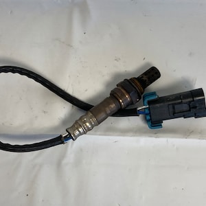 Może przedstawiać: Czarny i srebrny czujnik tlenu z czarnym kablem i niebieskim złączem.