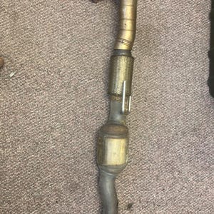 May include: A gold-colored catalytic converter with a metal mesh covering and a black exhaust pipe.