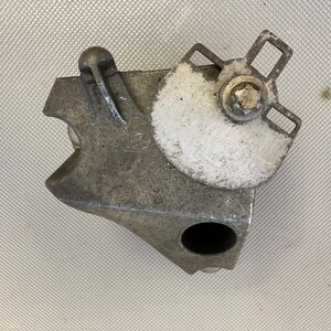 May include: A silver metal gear with a white painted section and a small metal knob. The gear has a hole in the center and a metal bracket with a screw.