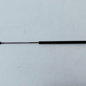 May include: A black metal gas strut support rod featuring a cylindrical main body and a thin, extendable piston rod. Each end of the component is finished with a small, flat circular mounting bracket containing a centered hole for attachment.