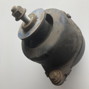 Peut inclure: Un support moteur automobile noir composé d'un boîtier en caoutchouc cylindrique, d'un boulon central fileté avec écrou et d'une rondelle circulaire plate. L'élément comprend un point de fixation secondaire avec un boulon et une base.