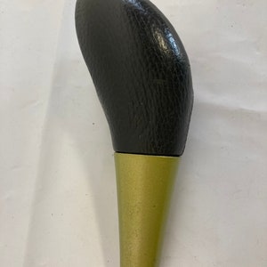 May include: A black leather gear shift knob with a gold metal base.
