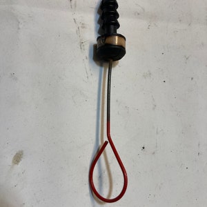 May include: A black and red automotive dipstick with a loop handle. The dipstick has a black plastic handle and a red loop at the end. The dipstick is used to measure the oil level in a vehicle's engine.