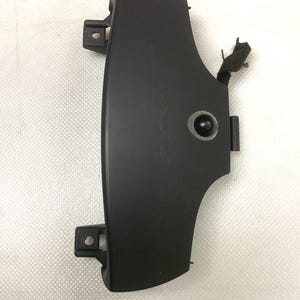 May include: Black plastic car part with a small round button and a wire attached. The part has two tabs on the side.