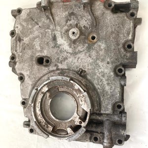 May include: A silver-colored metal engine part with a circular opening and multiple holes. The part is covered in dirt and grime.