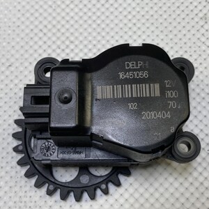 May include: A black automotive part with a gear-like component and a rectangular body. The part has the text "DELPHI 16451056" and a barcode. Additional text includes "12V", "1100", and "70".
