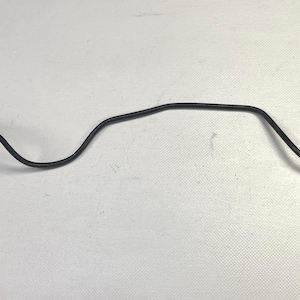 May include: A black electrical cable with a ring terminal on one end and a gray connector on the other. The cable is curved and lies on a white surface. This component is likely used in automotive or electronic applications.