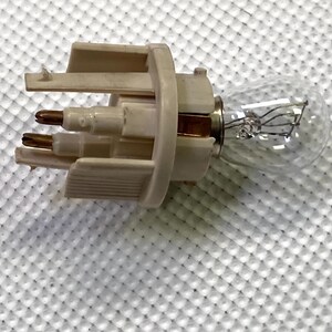 May include: A white plastic light bulb socket with three prongs. The socket is attached to a clear glass light bulb with a metal filament.