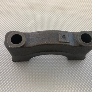 May include: A black metal crankshaft bearing cap with the number "4" stamped on it.
