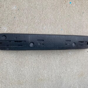 May include: Black plastic bumper reinforcement bar with multiple holes and slots.