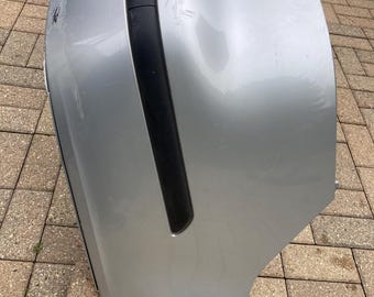 May include: Silver car bumper with black trim and the word "Aero" printed on the side. The bumper has some scratches and a red reflector. The bumper is likely a replacement part for a vehicle.