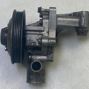 May include: A silver metal water pump with a black pulley. The pump has a hose connection and a metal bracket.