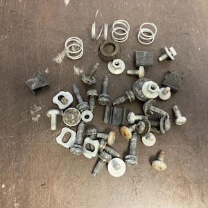 May include: A collection of silver metal screws, nuts, washers, and springs. Some of the pieces are black.
