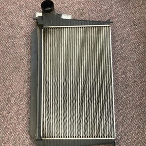 May include: A rectangular car radiator with a black frame and a silver core. The radiator has two black tubes and several small mounting tabs. The core is made of many thin, vertical metal fins.