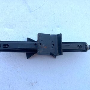 May include: A black metal scissor jack for automotive use, featuring a central lifting platform with a U-shaped bracket and a threaded rod mechanism on the side for manual operation. The tool has a matte finish with minor signs of wear.