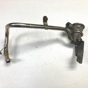 May include: A metallic automotive part with a curved pipe, a cylindrical component, and a bracket. The part has a silver finish with some areas showing signs of use. It is likely a component from a vehicle's engine or exhaust system.