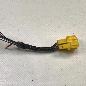 May include: A yellow electrical connector with multiple wires of various colors, including black, blue, and red. The wires are bundled together with black tape. The connector is on a white surface.