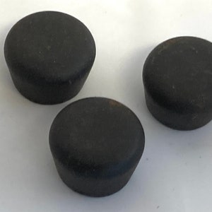 May include: Three dark gray, rounded bottle stoppers. Each stopper has a slightly tapered shape, with a wider top and a narrower base. The stoppers are made of a matte material and are arranged on a white surface.