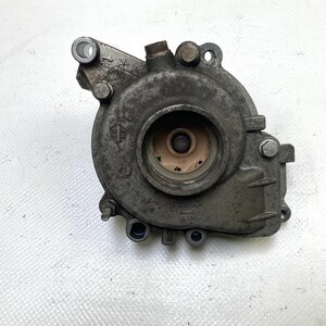 May include: A used, metallic gray automotive part with a circular central opening and multiple bolt holes. The part has a weathered appearance, with visible wear and tear, and is likely from a vehicle's engine or related system.