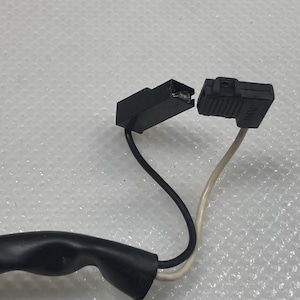 以下が含まれることがあります： 2つの黒い電気コネクタとワイヤー。1つは黒いワイヤー、もう1つは白いワイヤーです。コネクタは互いに近接して配置されており、接続されることを示唆しています。