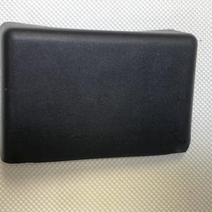 Peut inclure: Une boîte rectangulaire en plastique noir avec un dessus légèrement incurvé.