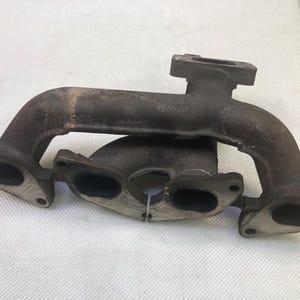 May include: A cast iron exhaust manifold with multiple ports and a textured surface.