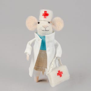 Op de afbeelding: Een witte viltmuis die een witte doktersjas draagt met een rood kruis op de hoed en een witte viltzak met een rood kruis.