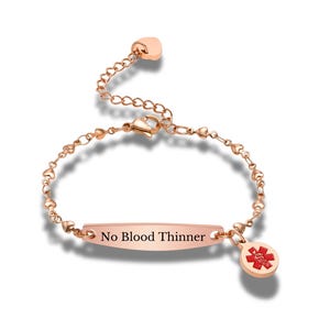 May include: Rose gold medical alert bracelet with a heart-shaped chain and a tag that reads "No Blood Thinner." A red medical symbol charm hangs from the bracelet.