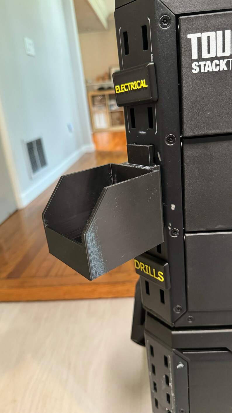 Puede incluir: Un sistema de almacenamiento de herramientas de metal negro con una bandeja de pl&aacute;stico negro etiquetada como "DRILLS". El sistema tiene una etiqueta que dice "ELECTRICAL" y otra etiqueta que dice "TOUGH STACK".