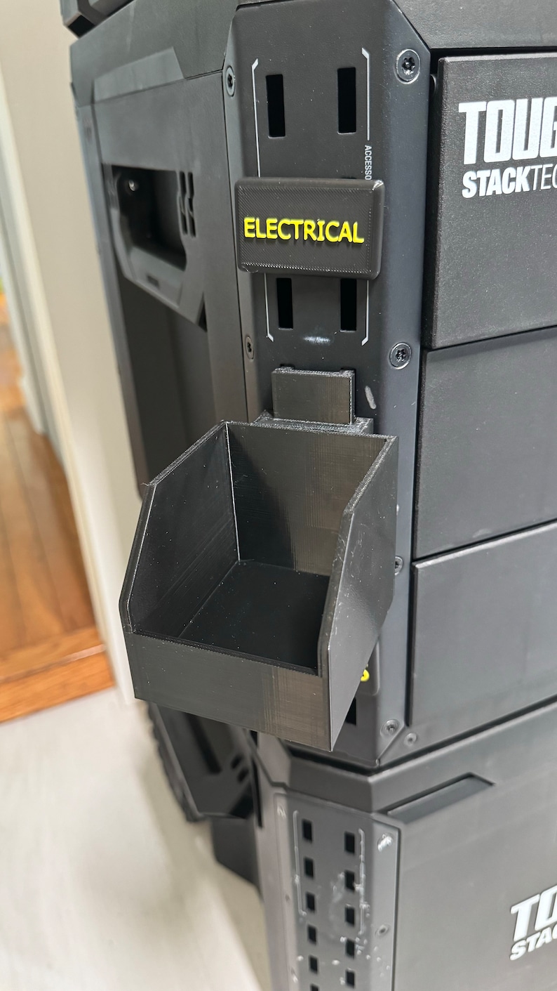Puede incluir: Caja de herramientas negra con un peque&ntilde;o contenedor de almacenamiento de pl&aacute;stico negro unido al lateral. La caja de herramientas tiene una etiqueta que dice "Electrical" en letras amarillas.