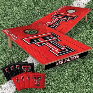 May include: A cornhole game set featuring two red wooden boards with a black and white Texas Tech logo and the text Texas Tech and Red Raiders. The set includes eight bean bags, four black and four red, each displaying the Texas Tech logo.