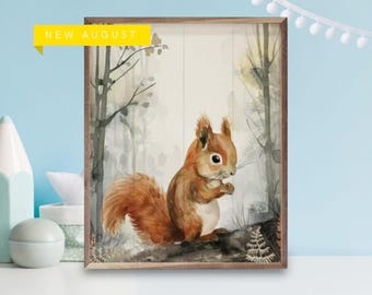 May include: A rectangular wall art print in a wooden frame featuring a watercolor illustration of a brown squirrel in a forest setting. A yellow banner in the top left corner contains the black text NEW AUGUST. The squirrel has a bushy tail.