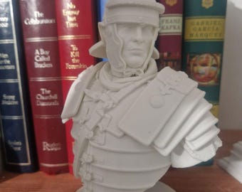 Pode incluir: Busto de um soldado romano impresso em 3D em branco, usando capacete e armadura. O busto está em uma base circular branca.