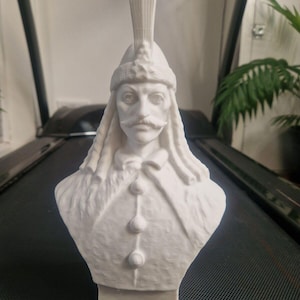 Può includere: Busto in scultura bianca di un uomo con barba e baffi che indossa un cappello piumato. La scultura è dettagliata con una superficie testurizzata ed è realizzata in materiale bianco.