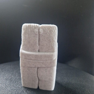 May include: A white ceramic sculpture of two figures embracing. The sculpture is textured and has a rough finish.