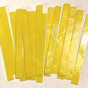 May include: A collection of bright yellow, rectangular strips arranged on a white surface. The strips appear to be made of a glossy material, possibly wax or a similar substance. The strips are of varying lengths.
