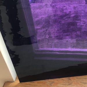 May include: A close-up of a purple glass panel with a dark border. The glass is slightly textured and has a subtle sheen. The panel is resting on a wooden surface.