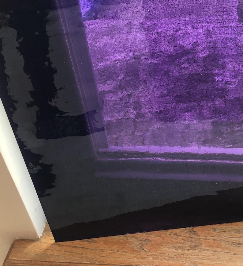Pu&ograve; includere: Primo piano di un pannello di vetro viola con un bordo scuro. Il vetro &egrave; leggermente testurizzato e ha una lucentezza sottile. Il pannello &egrave; appoggiato su una superficie di legno.