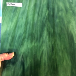 May include: A sheet of green stained glass with a swirling, marbled pattern. The glass has varying shades of green, creating a textured appearance. A small white label in the upper left corner reads "101-K3 U Green Opal".