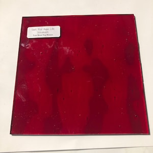 May include: A square piece of dark red glass with the text "Dark Red Aqua Lite Wissmach From Mixed Bag Mosaics" on a white label. The glass has a glossy finish and is set against a white background.