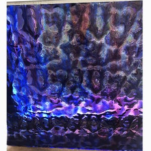 May include: Abstract artwork with a textured surface, featuring a blend of blue, purple, and pink hues. The piece has a rippled appearance, with light reflecting off the surface, creating a dynamic visual effect.